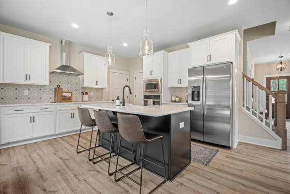 In the heart of Haley Meadows lies a modern kitchen featuring sleek white cabinets, an inviting island with stools, stainless steel appliances, and warm wood flooring.