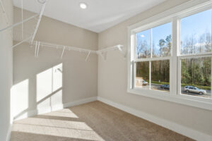 Empty walk-in closet with beige carpet, white wire shelving on two walls, and a window showing a view of the outdoors with cars and trees.