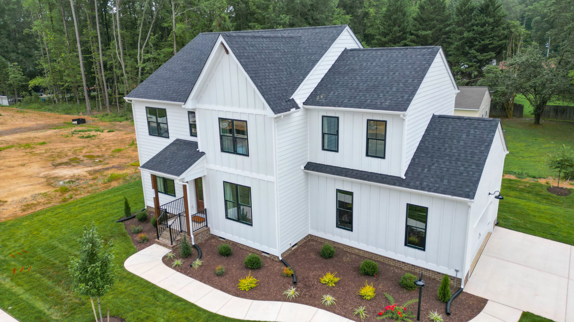 Aerial view of a modern white two-story house in Haley Meadows, featuring a landscaped yard and surrounding greenery.