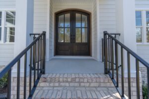 A front entrance with brick steps, black railings, and double arched wooden doors on a white-paneled house.