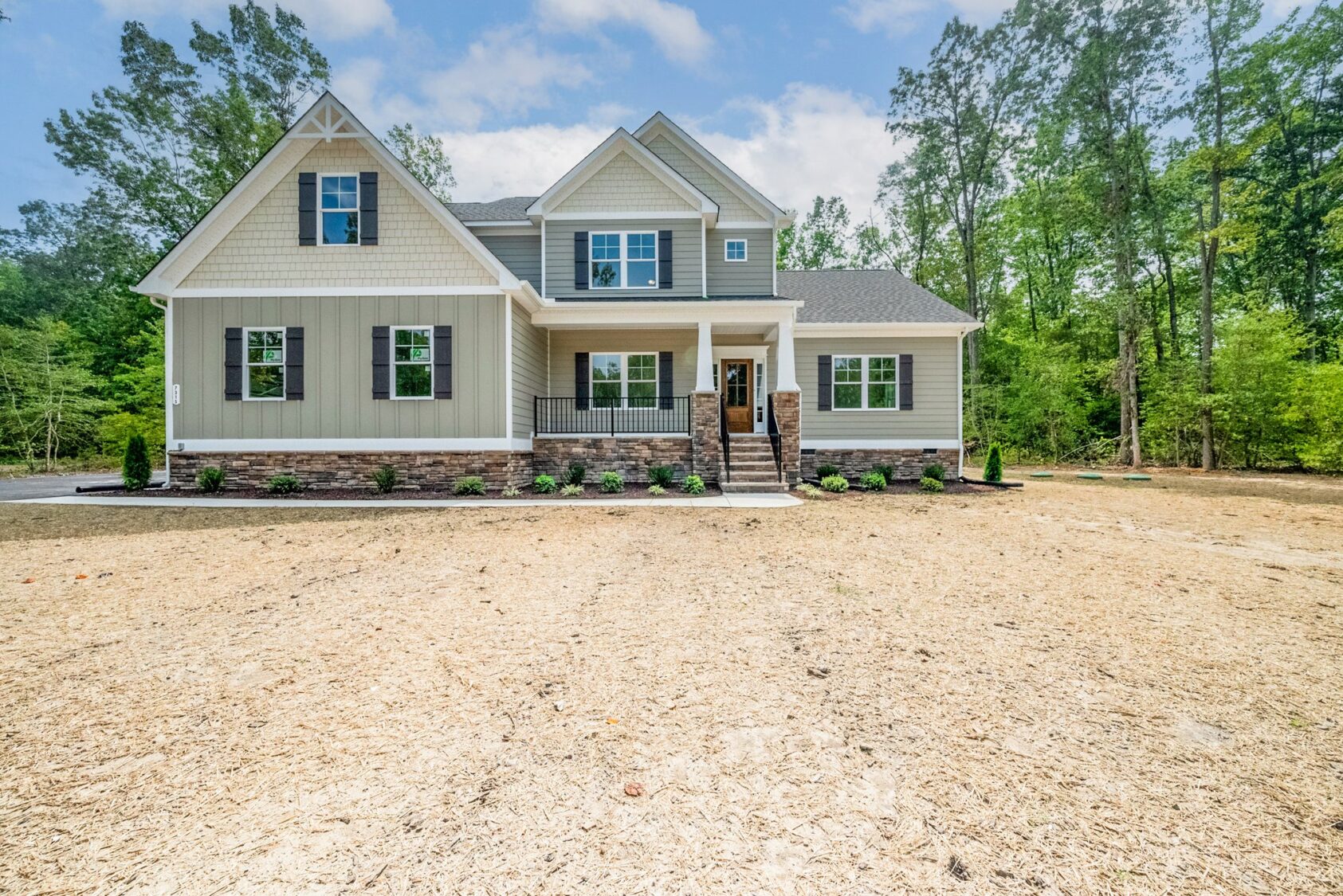 A modern new home in Virginia, this two-story house features a stone porch, surrounded by trees and a spacious dirt yard.