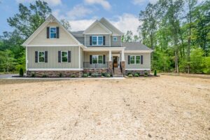 A modern new home in Virginia, this two-story house features a stone porch, surrounded by trees and a spacious dirt yard.