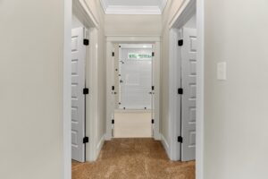 Carpeted hallway with white doors leading to a well-lit bathroom featuring a glass shower door.