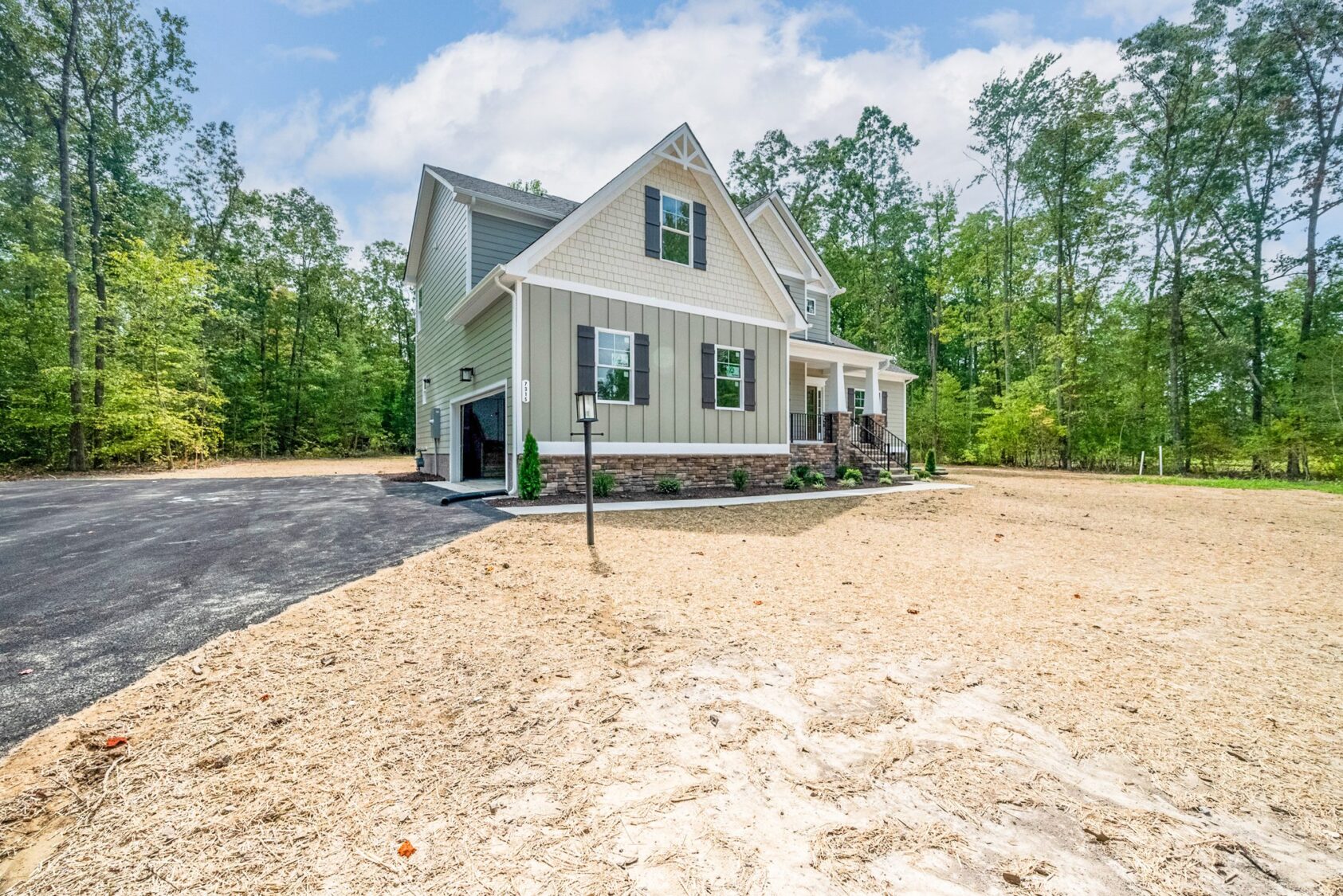 Charming new home with stone foundation, nestled among trees and a newly paved driveway under a clear sky.