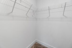 Empty walk-in closet with white walls and wire shelves on two sides, and beige carpet flooring.