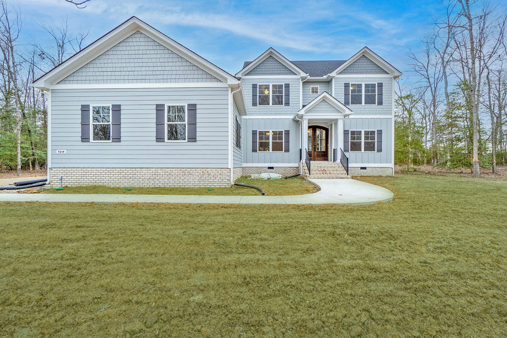 This large gray Manchester house features elegant white trim, black shutters, and a welcoming front porch. It's beautifully situated amidst a spacious grassy yard, offering both charm and serenity.
