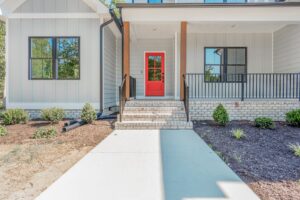 Modern house entrance with a bright red door, brick steps, black railing, and landscaped front yard.