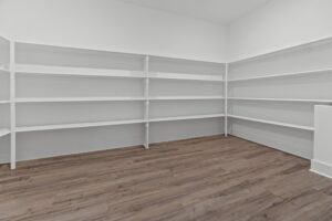 Empty room with wooden floors and white walls, featuring built-in white shelves on two walls.