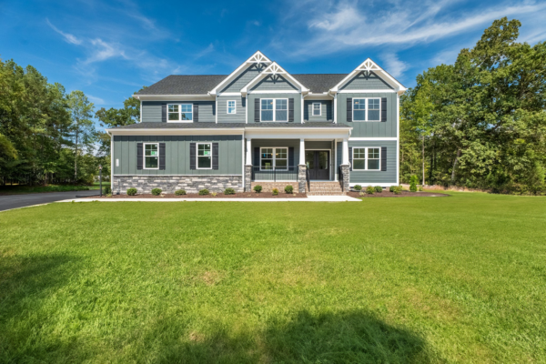 A large gray and white house with a gabled roof, reminiscent of Savannah, is surrounded by lush green lawns and trees.