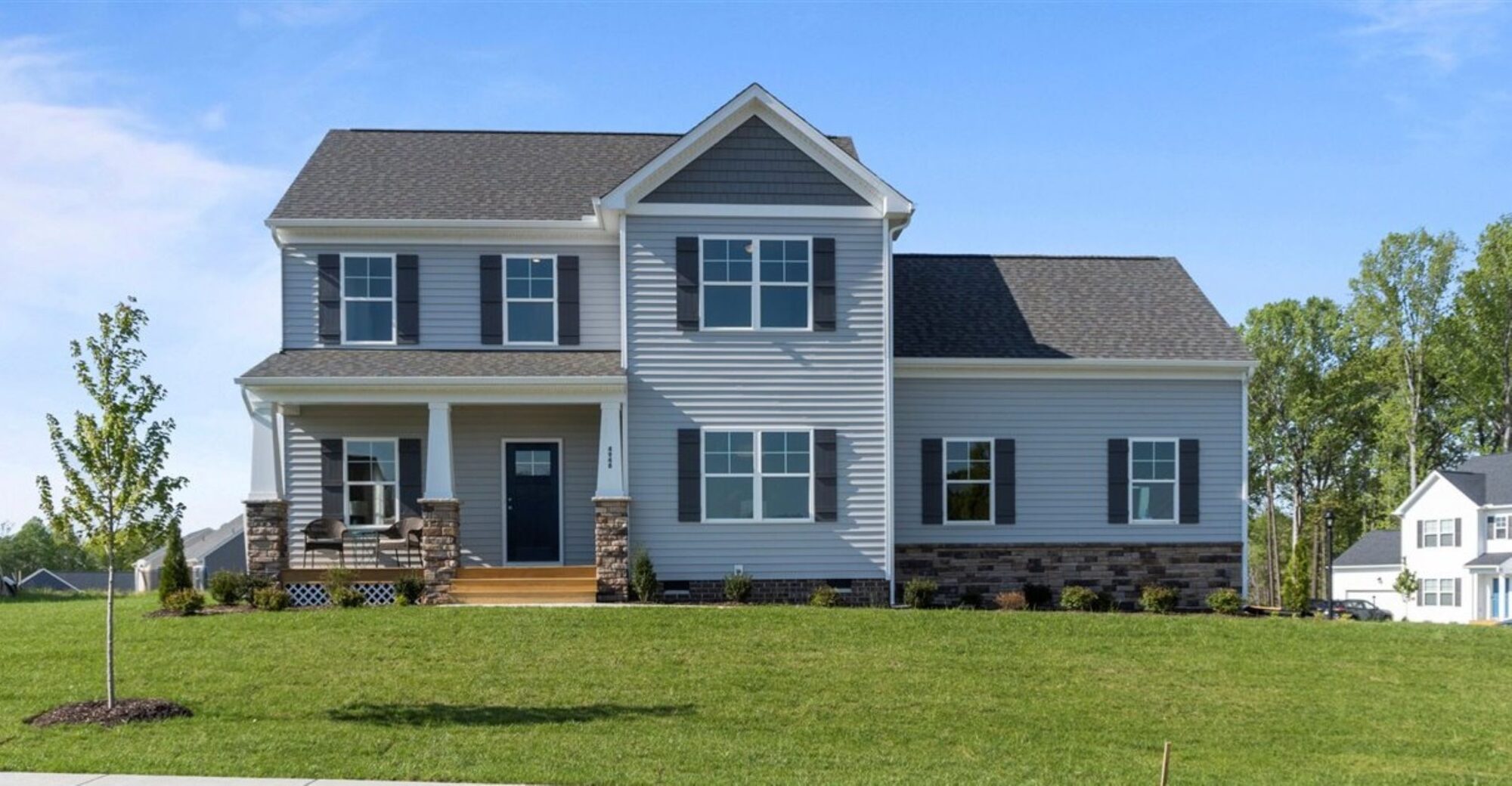 Two-story grey house in Poplar Village, with a porch and manicured lawn, set against trees and a clear Rowland sky.