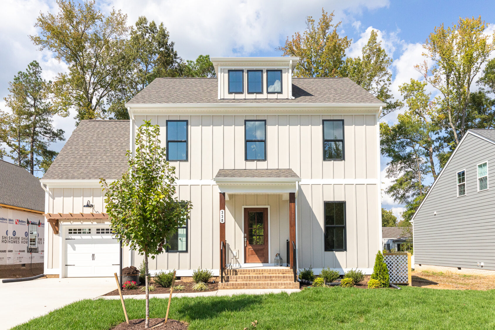 The two-story modern house on Lot 5 in Haley Meadows features a sleek white exterior, a spacious garage, and a charming small tree gracing the front yard on this sunny day.