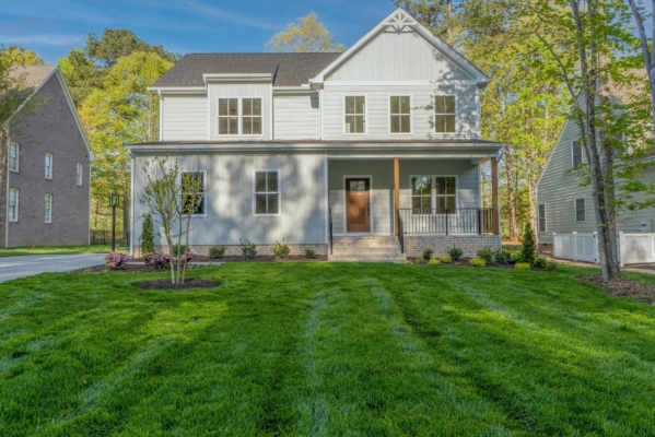 Two-story white house with a wooden porch, nestled under a clear blue sky in the lush greenery of Richmond.