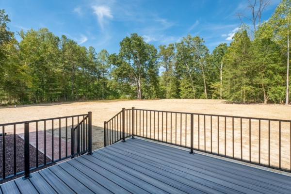 View from a deck with black railing, overlooking a large field and trees under the clear blue sky of new homes in Virginia.