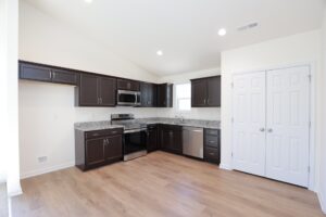 Modern kitchen with dark cabinets, stainless steel appliances, and light wood flooring.
