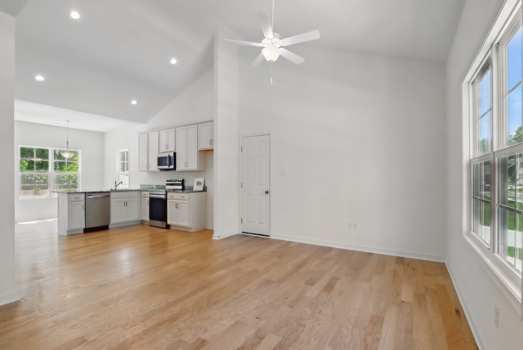 Bright, modern kitchen and living area with wood floors, white walls, and large windows letting in natural light.