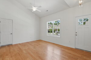Bright, empty room with wood floors, white walls, ceiling fan, window, and a door to the outside.