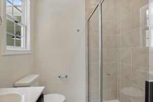 Modern bathroom with a glass shower, white toilet, tiled walls, and a window letting in natural light.