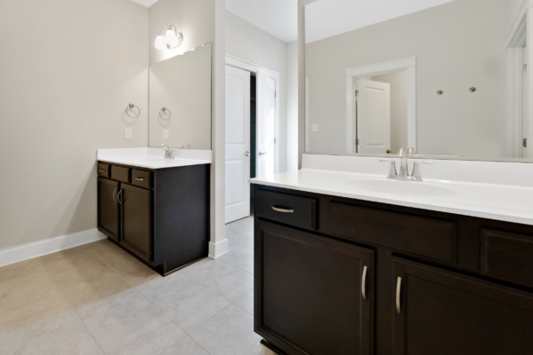 Modern bathroom in a new home with two dark wood vanities, large mirrors, light walls, and a tile floor.