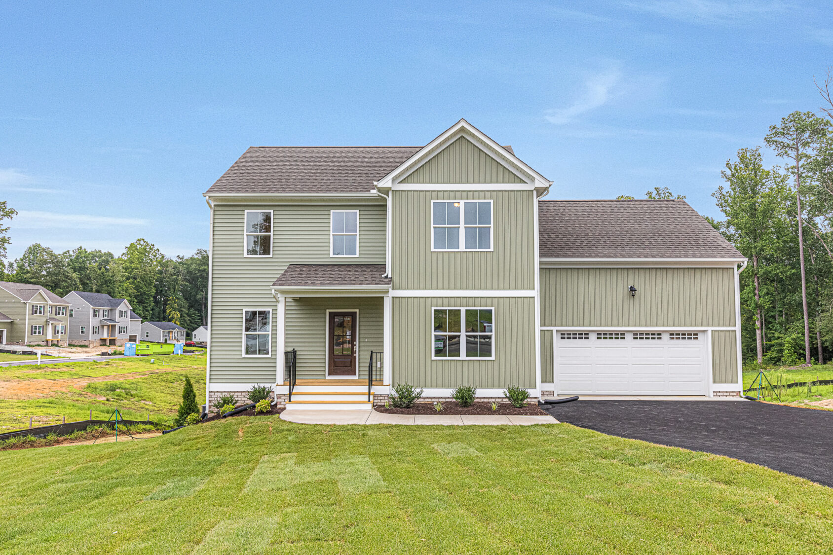 Light green two-story house with a garage in Poplar Village, Lot 22, featuring a porch and a well-kept lawn.