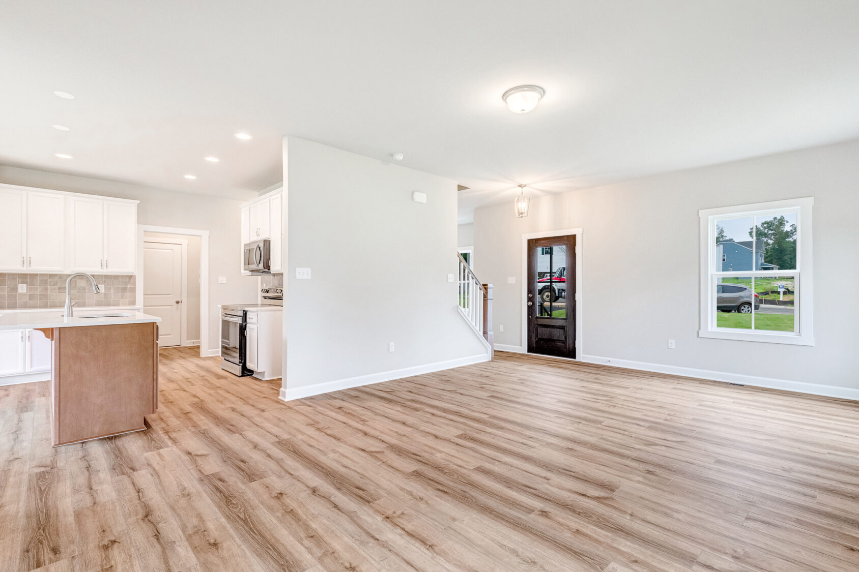 Bright, empty open-plan living area in Poplar Village Lot 22 with wood floors, white kitchen, and natural light.