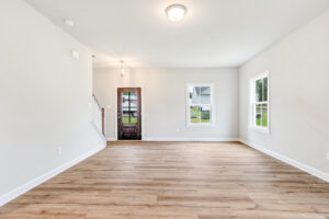 Bright, empty room in Poplar Village with light wood floors, white walls, windows, and a door near a staircase.