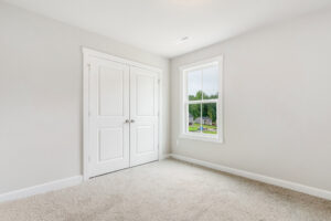 Empty room in Poplar Village with beige carpet, double closets, and a window offering a suburban view.