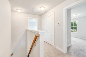 Bright hallway at the top of stairs in Lot 22, Poplar Village, with white doors, beige walls, and carpeted floors.