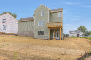 A newly built green house with a raised deck on sloped Lot 22 in Poplar Village, straw covering the bare backyard.