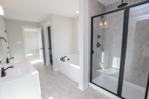 Modern bathroom in Lot 81, Anderson Court, with double sinks, a bathtub, and a glass-enclosed shower with black fixtures.