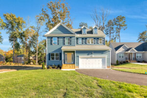 Two-story blue house with white trim and garage on sunny, grassy