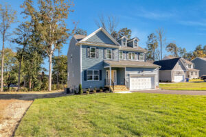 Charming two-story blue home, featuring white trim, garage, and lush green lawn.