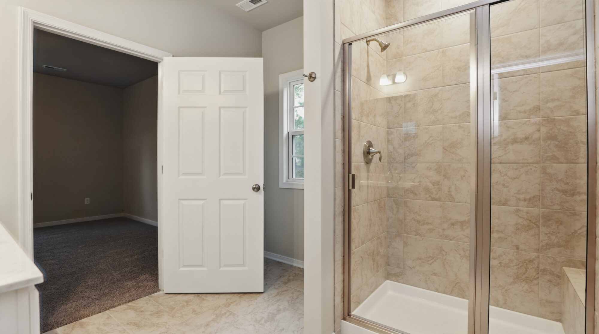 Bathroom with glass shower, beige tile, and white door open to adjoining carpeted Somerset Hill room.