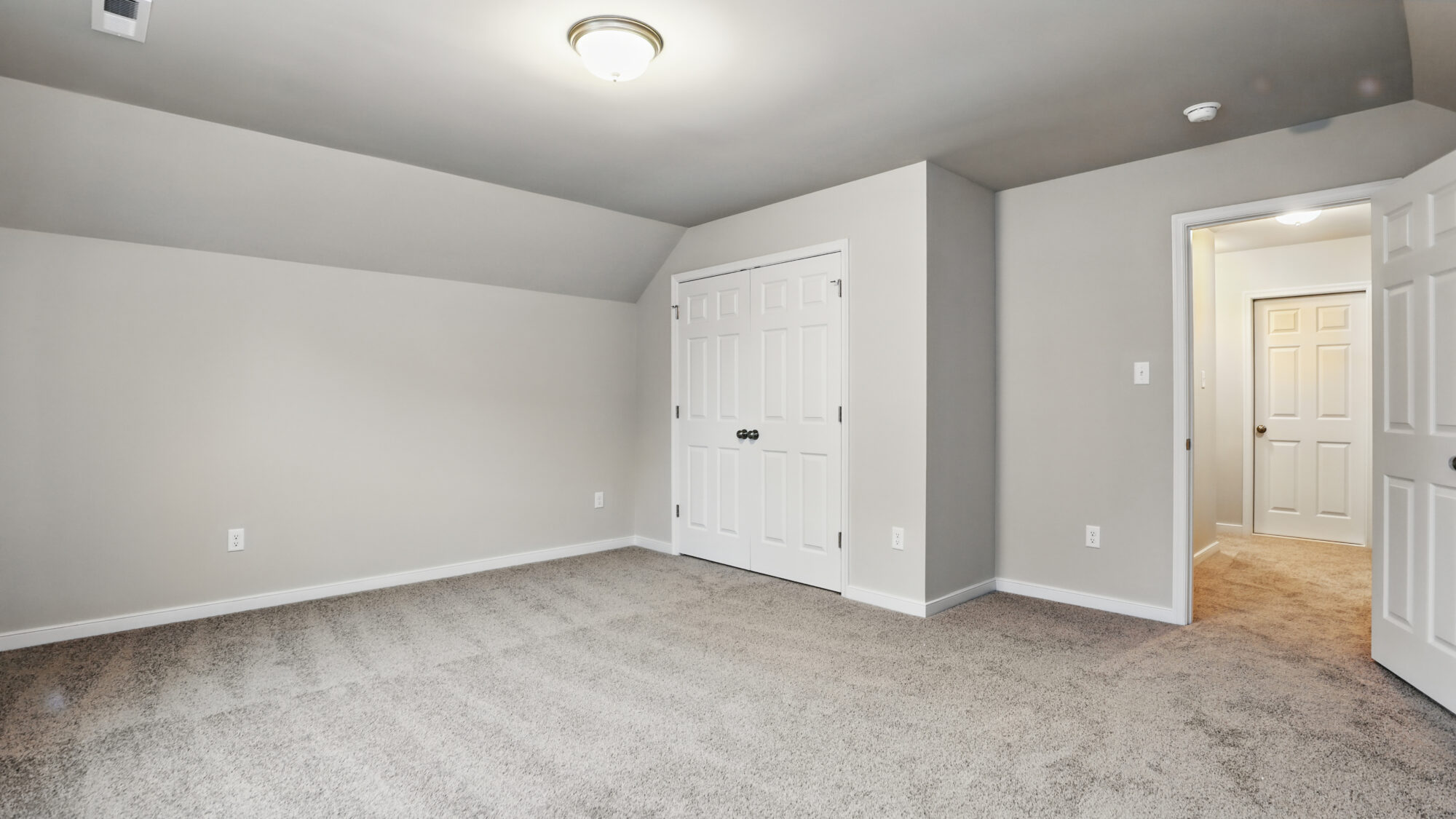 Empty carpeted bedroom with gray walls in Somerset Hill, ceiling light, double closet doors, and open door to hallway.