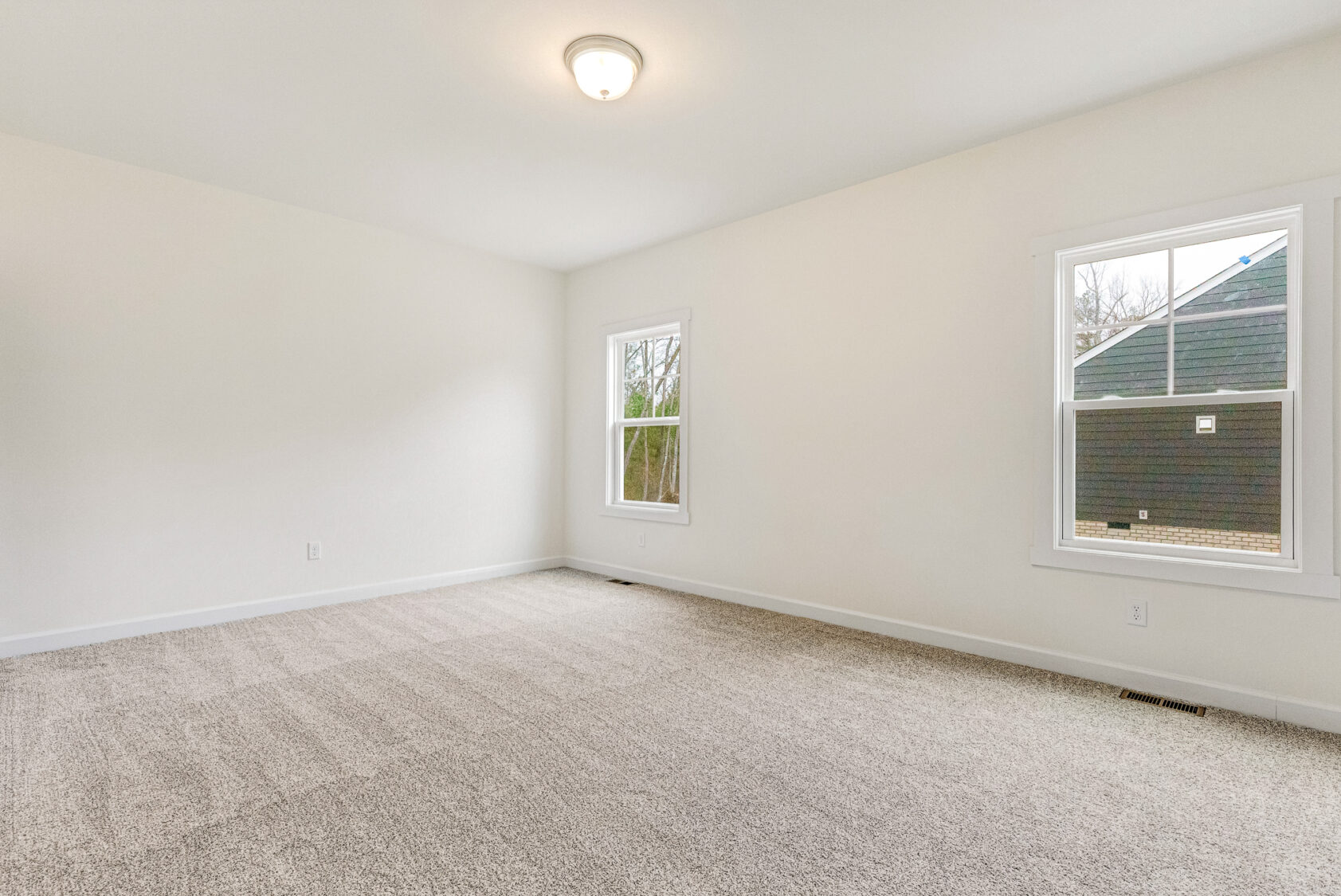 Empty room in Somerset Hill with beige carpet, white walls, ceiling light, and two windows framing the view outside.