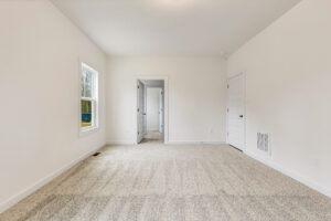 Empty, carpeted room with white walls in Somerset Hill; features a window and two white doors, one to the bathroom.
