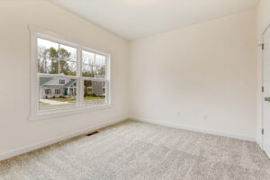Empty room at Somerset Hill with light walls, carpeted floor, and a window overlooking houses and trees.