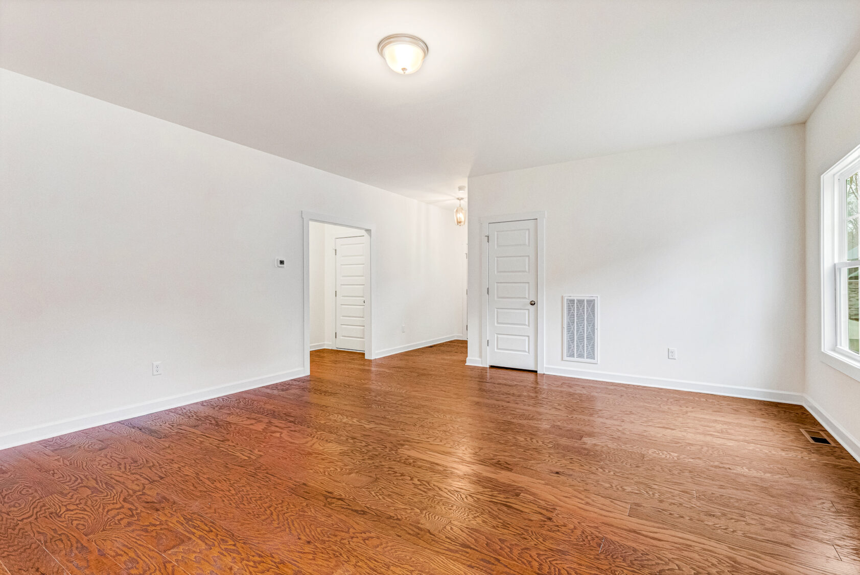 Bright empty room with hardwood floors at Somerset Hill, white walls, multiple doors, and a window letting in natural light.