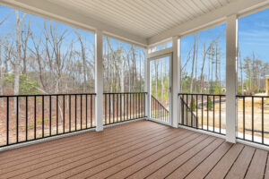 Screened-in porch with wood decking, white trim, and black railing overlooks Somerset Hill's wooded backyard.