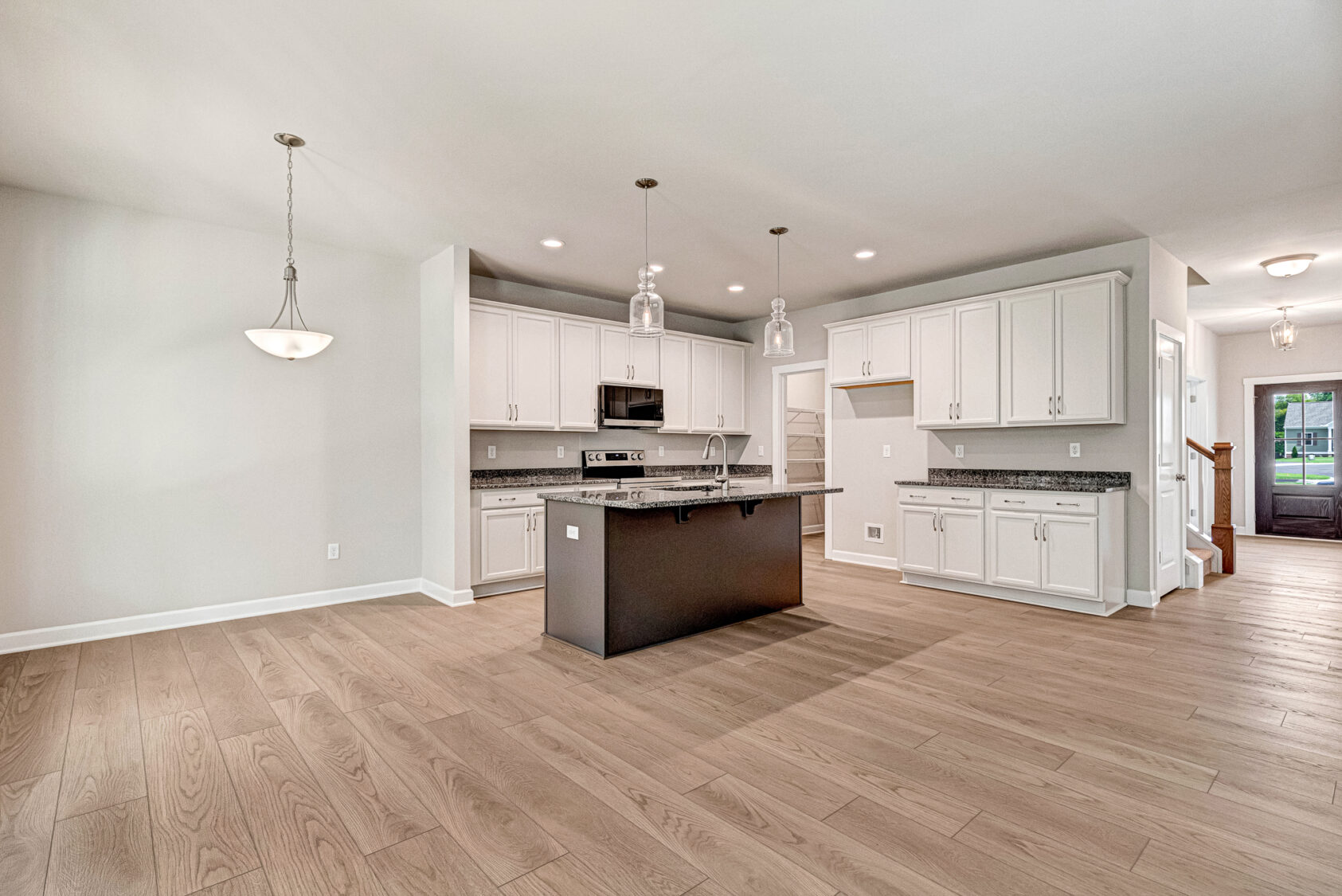 Modern kitchen in Somerset Hill Lot 5 with white cabinets, a dark central island, and wood-look flooring.