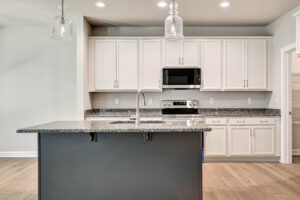 Modern Lot 5 kitchen featuring white cabinets, a dark gray island, granite countertops, and two glass pendant lights.