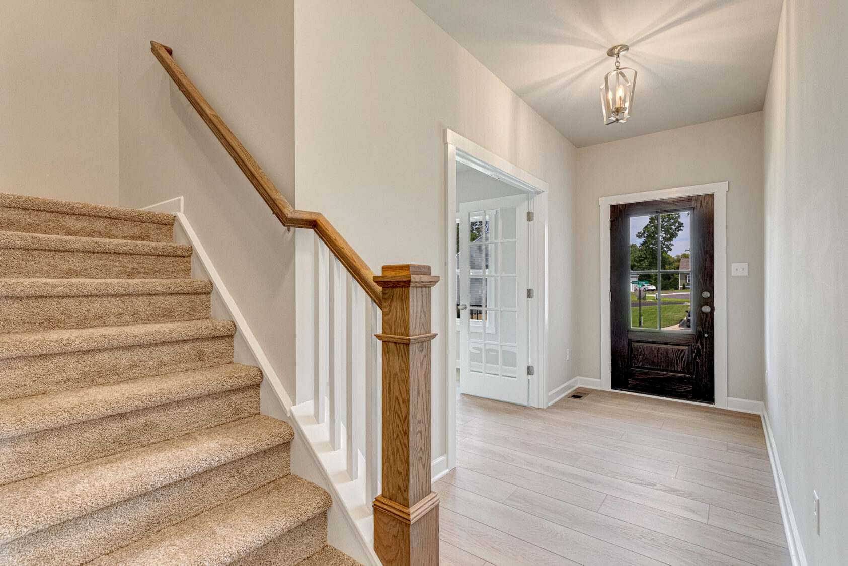 Foyer of the Somerset Hill property with carpeted stairs, a wooden railing, and a dark front door.